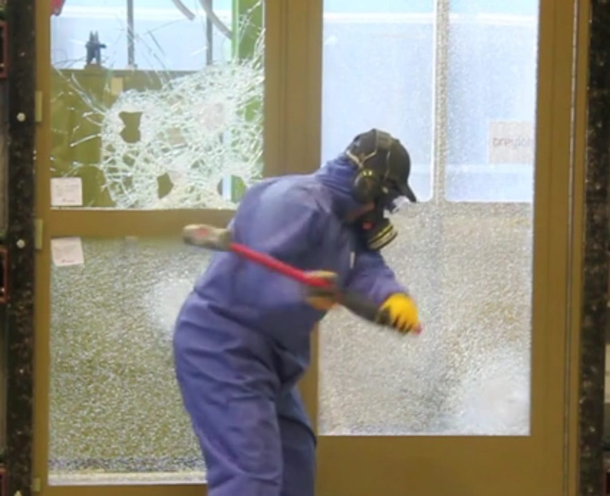 BRE Tester hitting Warrior Door with a sledgehammer. Glass shows cracks but no holes.
