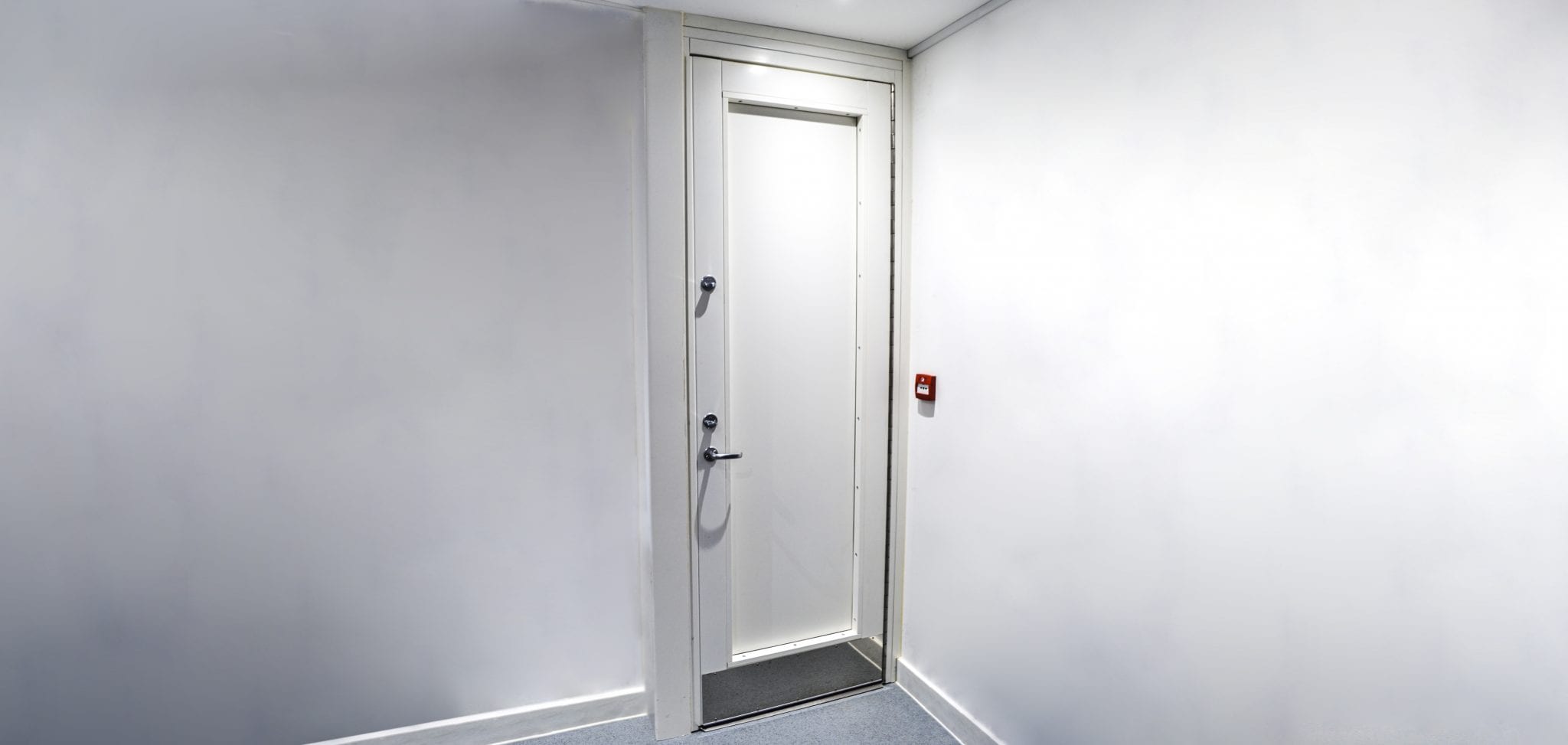White fully stainless-steel Warrior Safe Room Door in a white room.