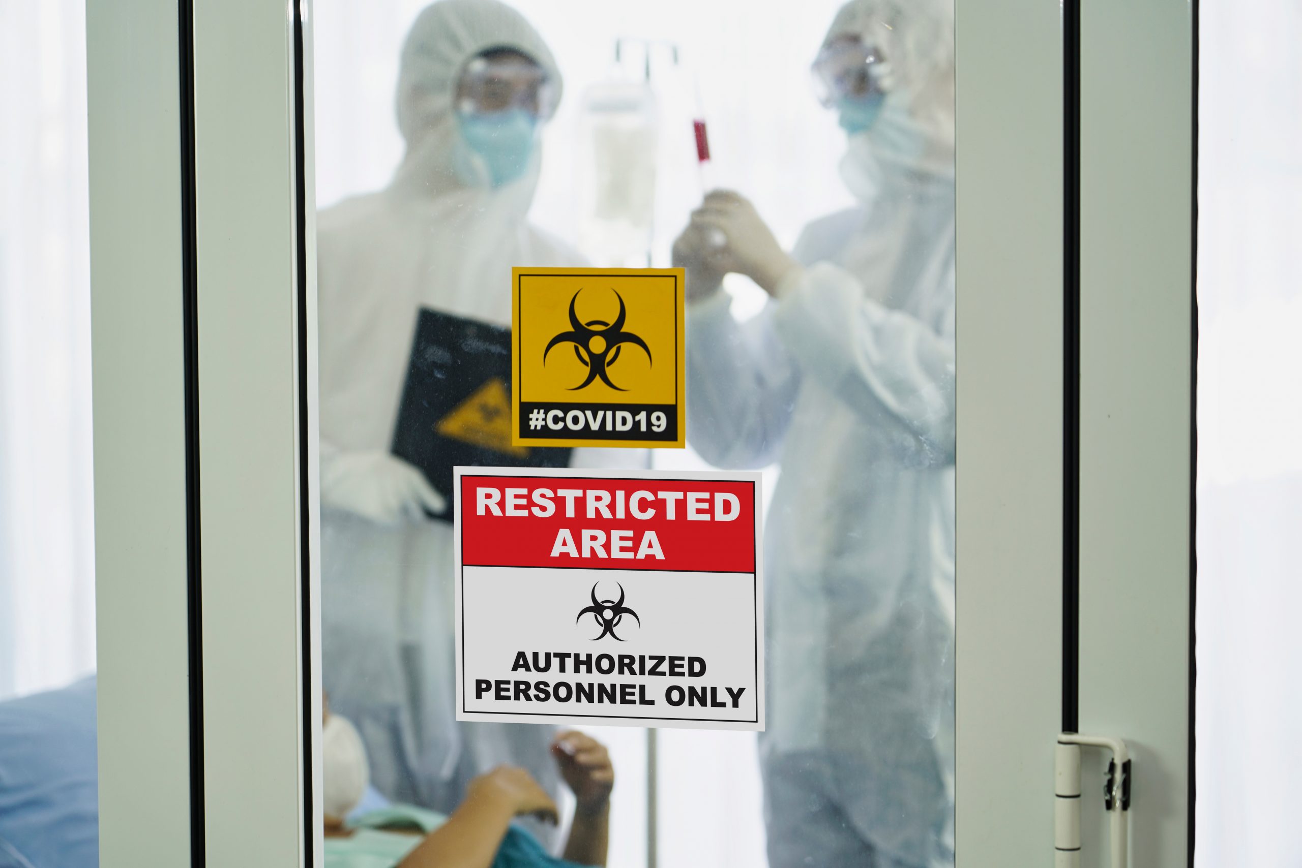 Patient and two doctors in full ppe behind a door in a hospital with restricted access and covid outbreak signs
